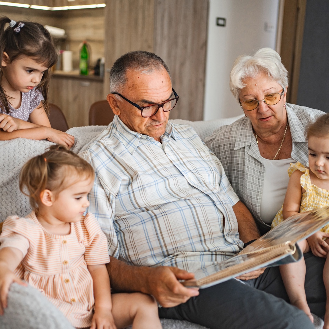 Oma en opa in hun rol als grootouders tijdens een voorleesmoment met hun kleinkinderen op de zetel